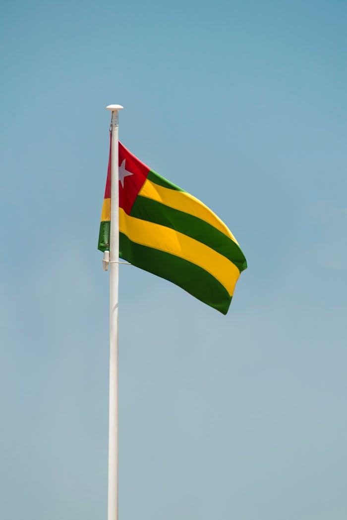 services-04 A striking image of the Togo national flag waving against a clear blue sky in Lomé, Togo.